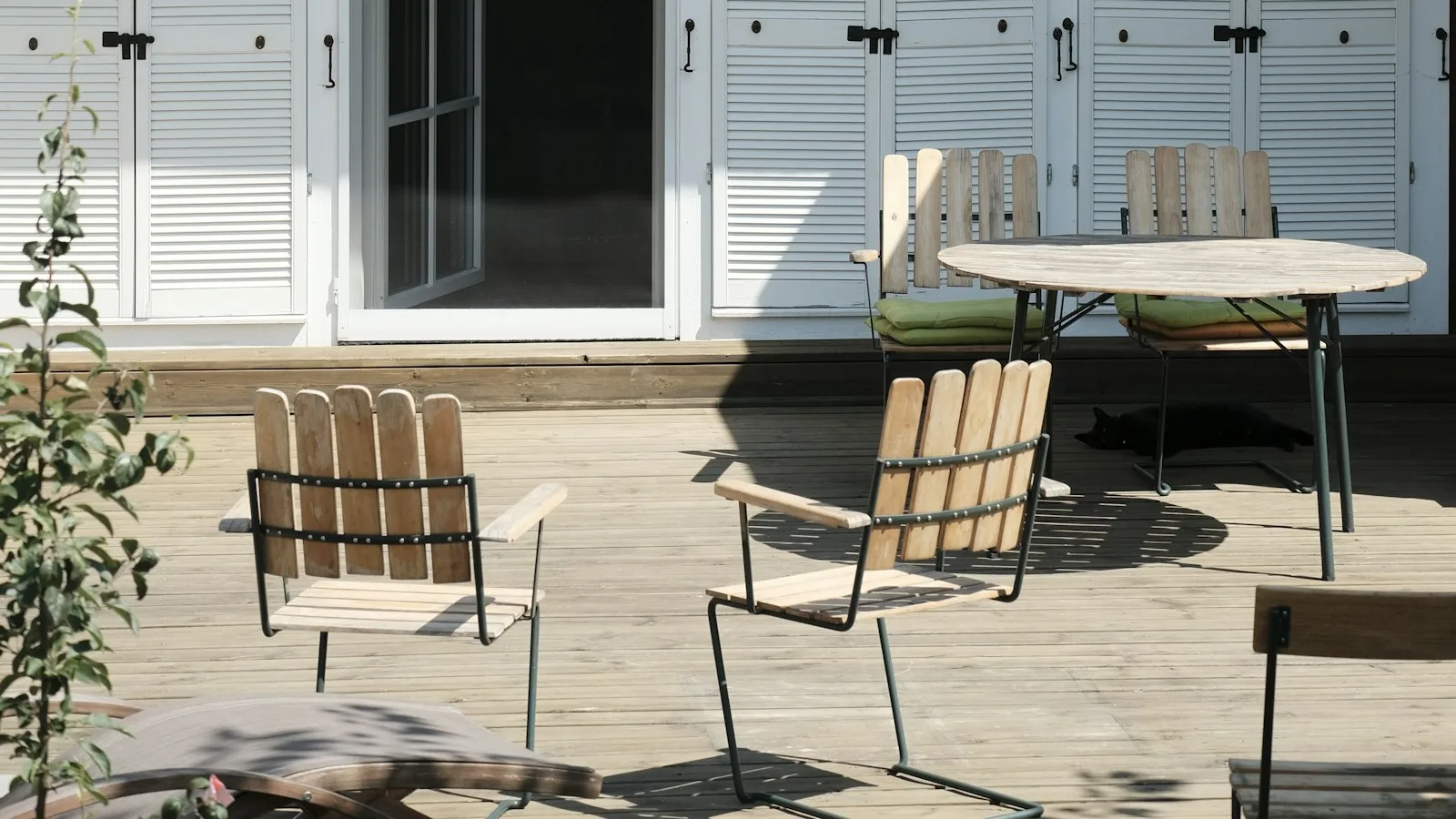 Patio chairs and a table beside an open glazed doorway and white shutters