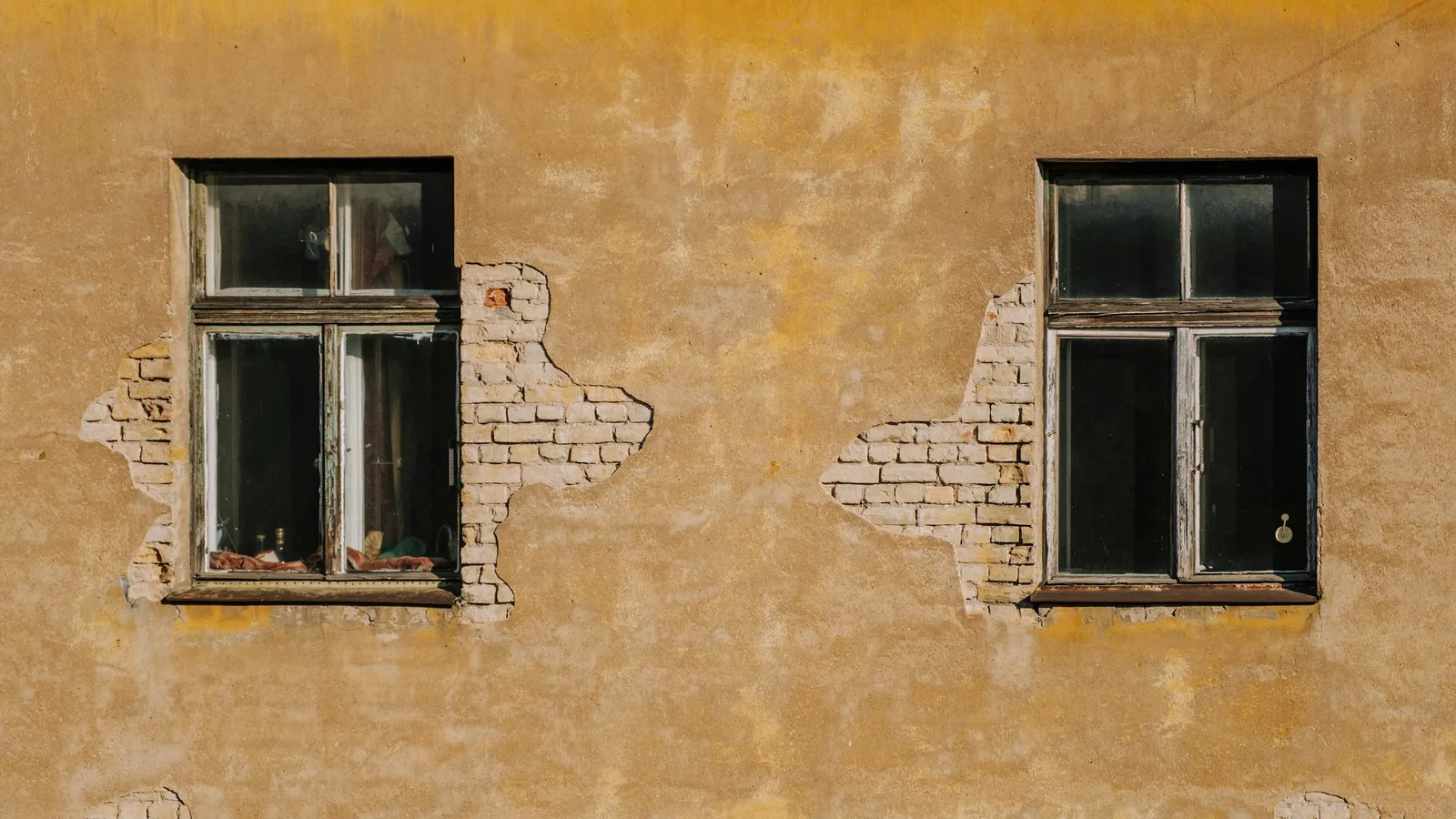 Two adjacent aging windows set into a weathered exterior wall