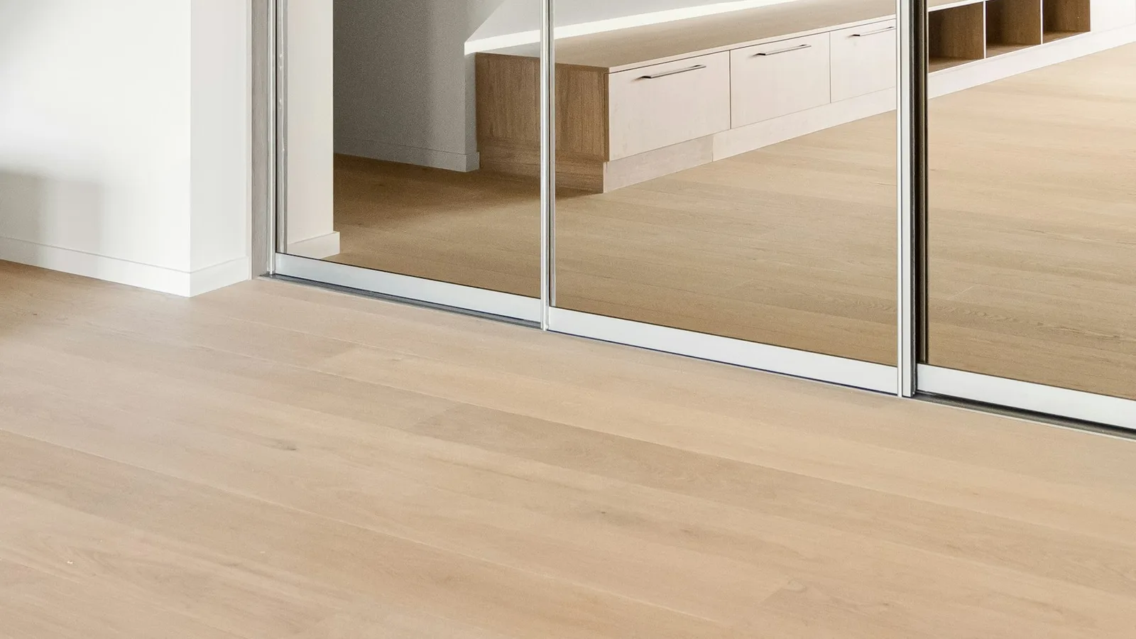 Floor-level track beneath glazed sliding panels beside a wood floor